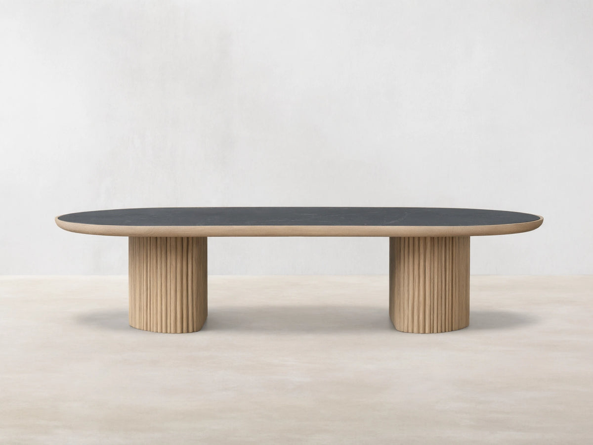 Astor Coffee Table with an oval marble top, supported by two cylindrical wooden bases wrapped in oak reeds, against a wooden floor.