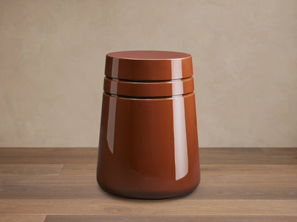 August Lacquer Stool with a high-gloss finish in a warm brown color, featuring a smooth, tapered cylindrical shape on a wooden floor.