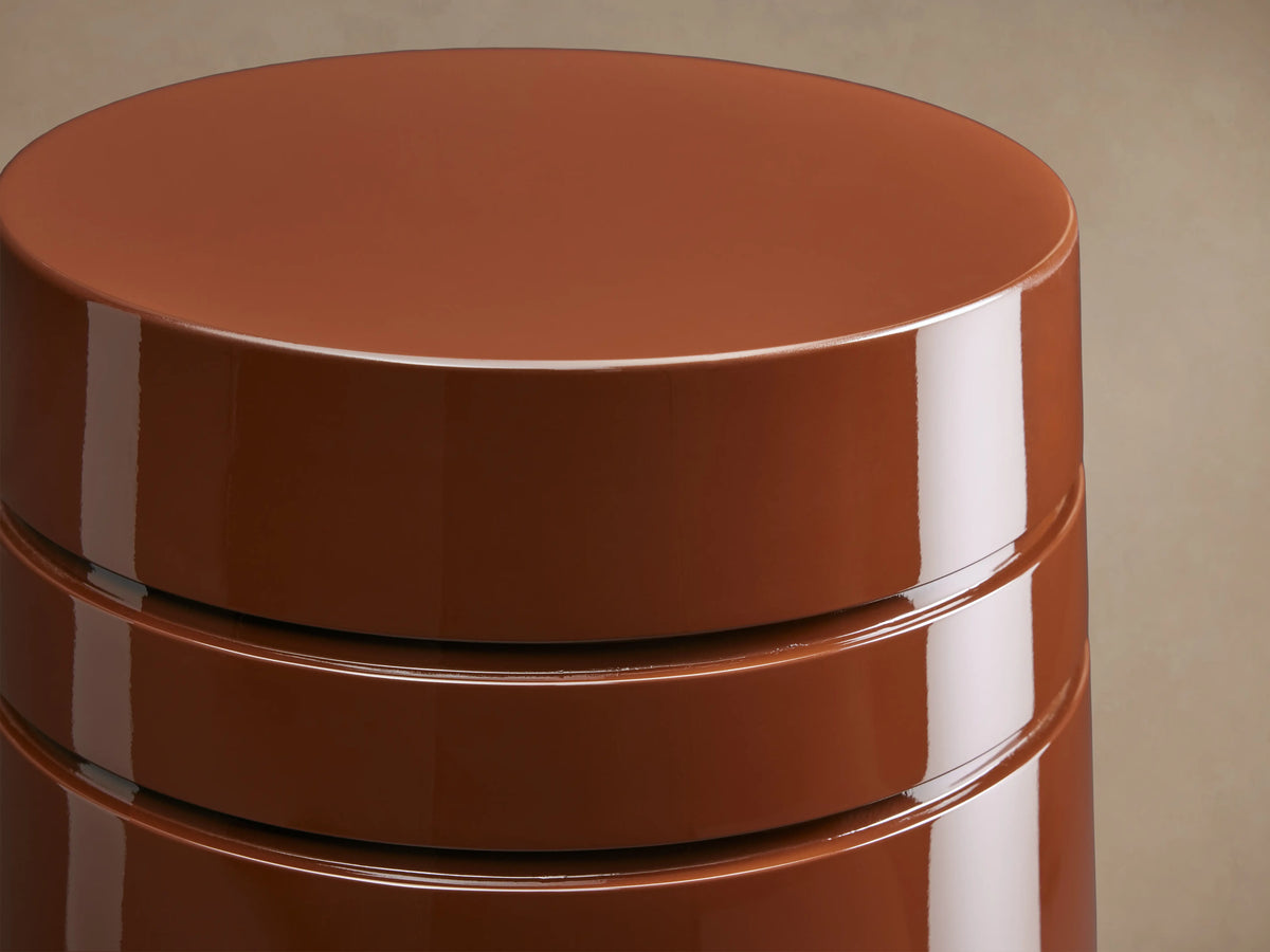 August Lacquer Stool with a high-gloss finish in a warm brown color, featuring a smooth, tapered cylindrical shape on a wooden floor.