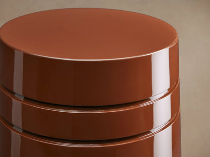 August Lacquer Stool with a high-gloss finish in a warm brown color, featuring a smooth, tapered cylindrical shape on a wooden floor.