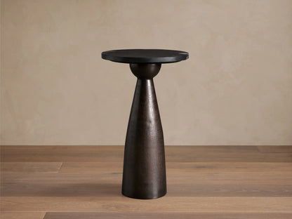 Beaufort Outdoor Martini Table with a dark mottled bronze conical base and a black round top, set on a textured stone floor.