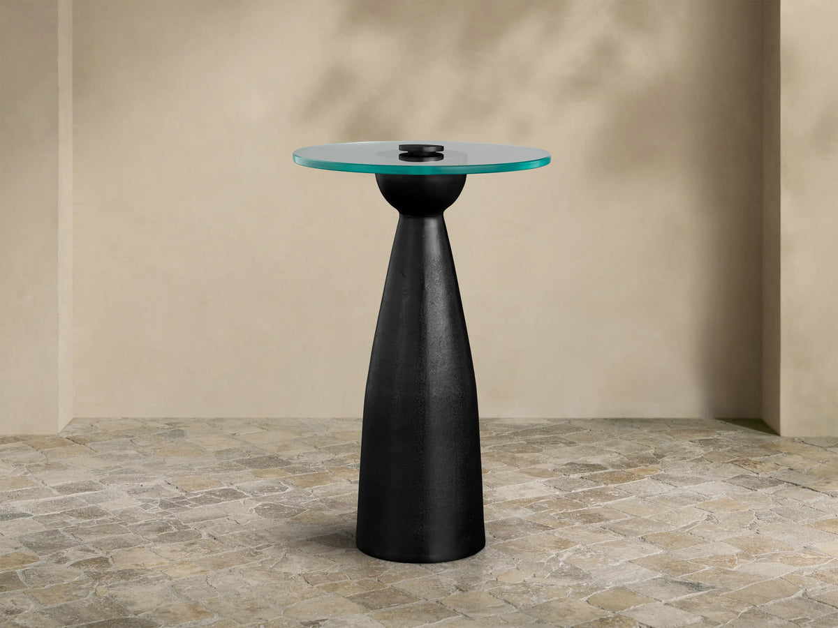 Beaufort Glass Top Martini Table, round glass top with faint green tint, on a dark, tapered pedestal base. Set on light stone floor.