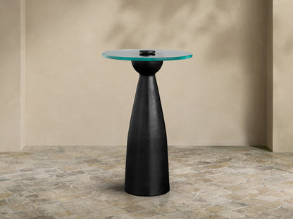 Beaufort Glass Top Martini Table, round glass top with faint green tint, on a dark, tapered pedestal base. Set on light stone floor.