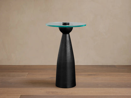 Beaufort Glass Top Martini Table, round glass top with faint green tint, on a dark, tapered pedestal base. Set on light stone floor.