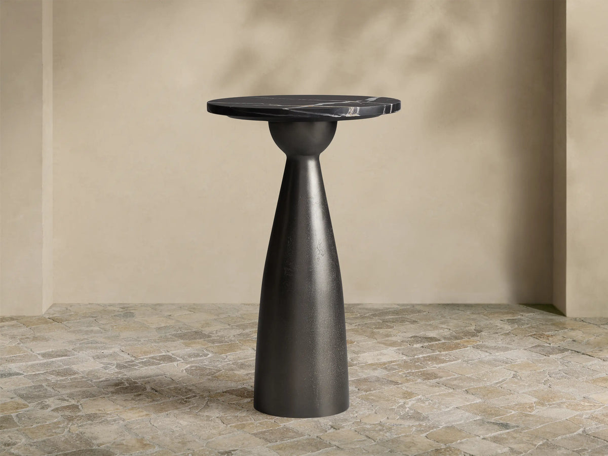 Beaufort Martini Table: round black marble top with white veining on a dark, textured conical base, sitting on stone tiles.