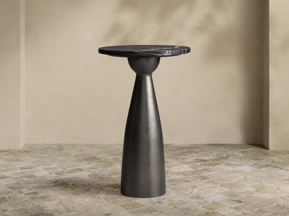 Beaufort Martini Table: round black marble top with white veining on a dark, textured conical base, sitting on stone tiles.