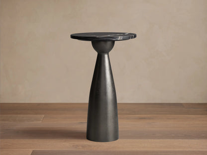 Beaufort Martini Table: round black marble top with white veining on a dark, textured conical base, sitting on stone tiles.