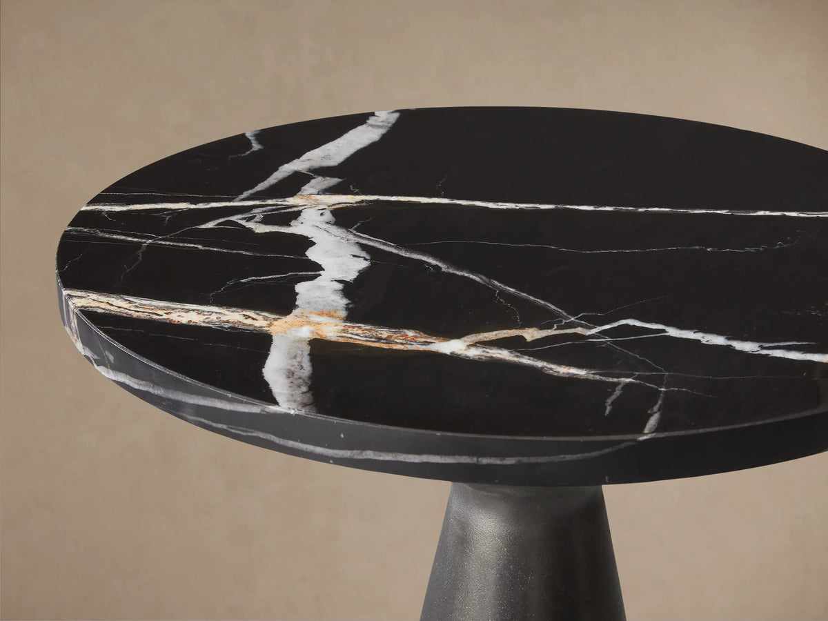 Beaufort Martini Table with round black marble top & white veining, dark graphite conical base, against beige wall & wood floor.