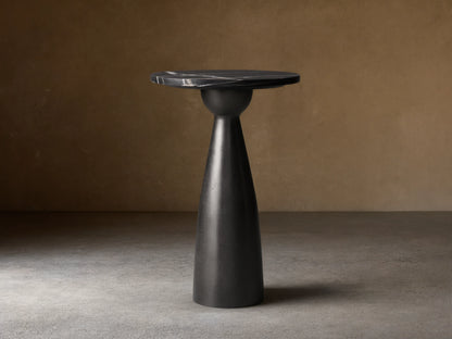 Beaufort Martini Table: round black marble top with white veining on a dark, textured conical base, sitting on stone tiles.