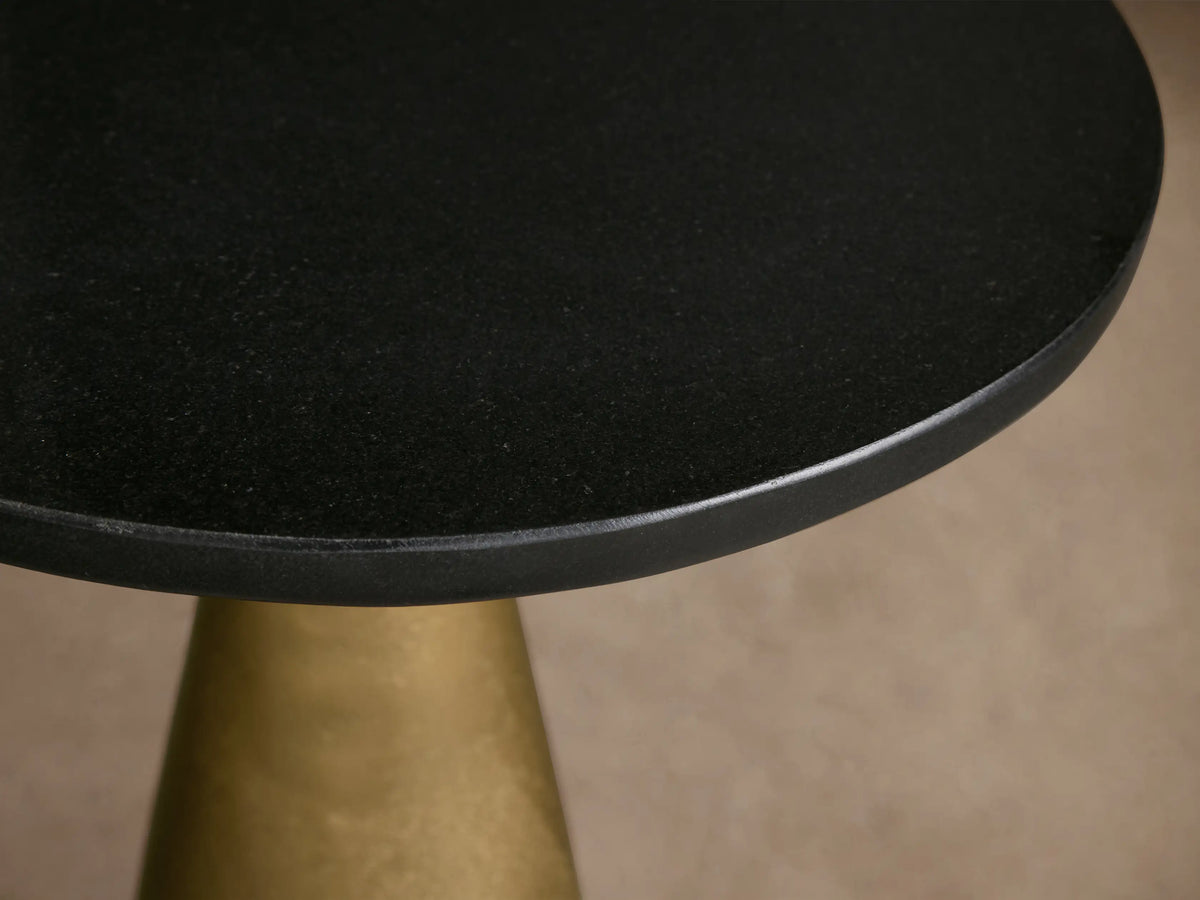 Front view of the black top Beaufort Martini Table with an antique brass conical base on a tiled floor.