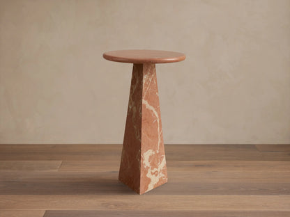 Brecken Martini Table with round top and angular, tapered base made of reddish-brown marble with white veining on wood floor.