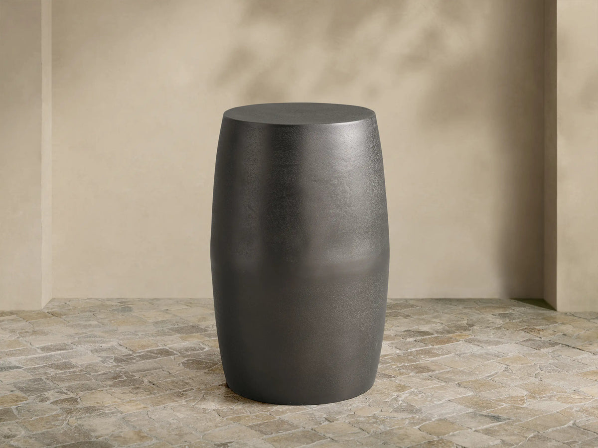 Antiqued dark gray Hammered Drum End Table with a textured finish, standing on a tiled floor against a light beige wall.