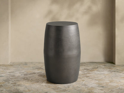 Antiqued dark gray Hammered Drum End Table with a textured finish, standing on a tiled floor against a light beige wall.