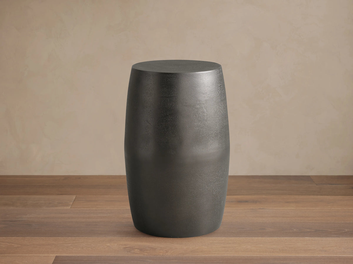Hammered Drum End Table made of dark artisan-cast aluminum with a smooth, curved surface and antiqued finish on a wooden floor.