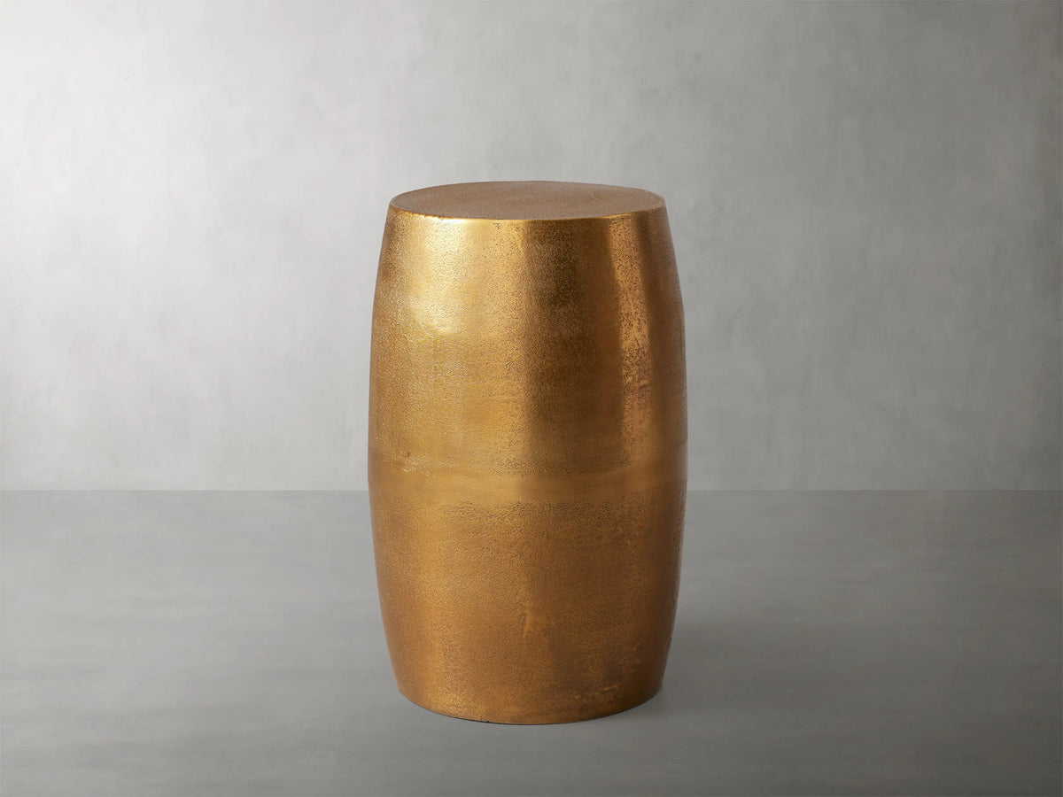 Hammered Drum End Table with an antiqued metallic gold finish and hand-pounded texture, standing upright against a grey background.