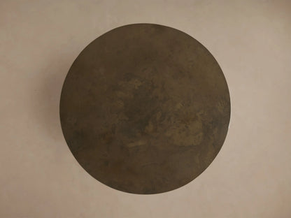 Bruna End Table, cylindrical, close-up. Dark, weathered metal with rich brown and bronze organic patina and texture.