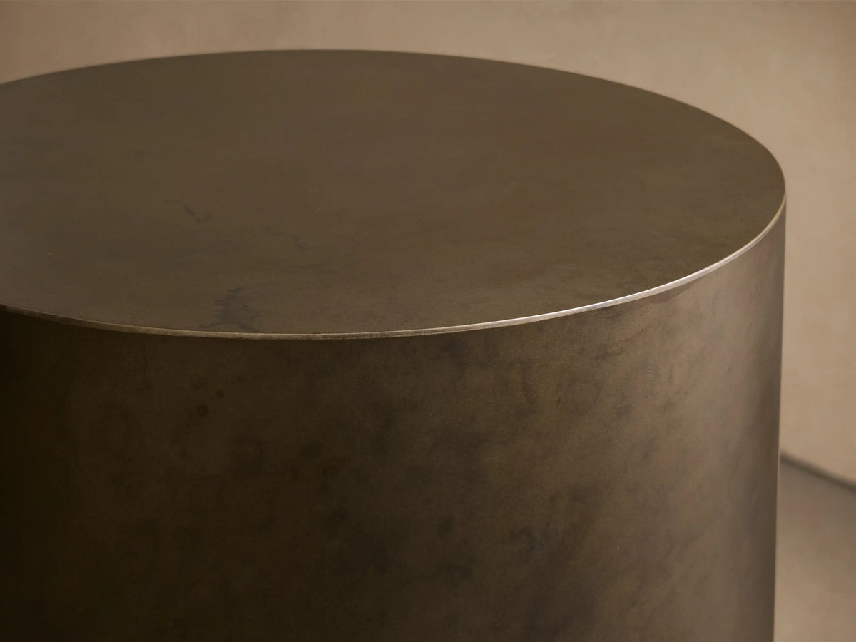 Front view of the dark bronze cylindrical Bruna Pedestal with a weathered metallic patina, on a wooden floor.
