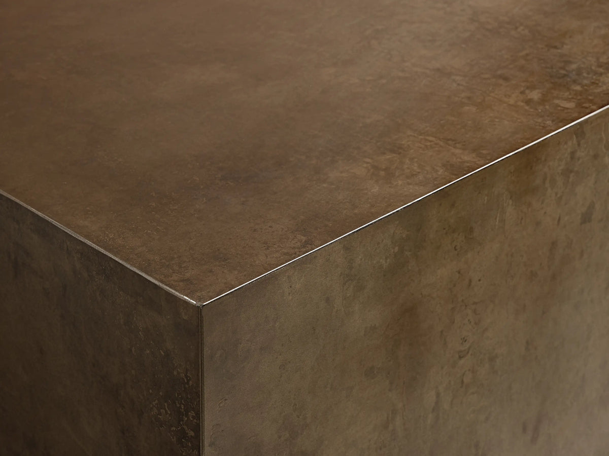 Angled view of a rectangular coffee table featuring a distressed bronze body, a dark top, and a subtle metallic silver trim.
