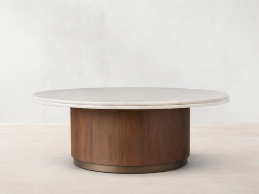 Caden Round Coffee Table with a cream stone top, walnut wood veneer cylindrical base, and antique bronze plinth on wood floor.