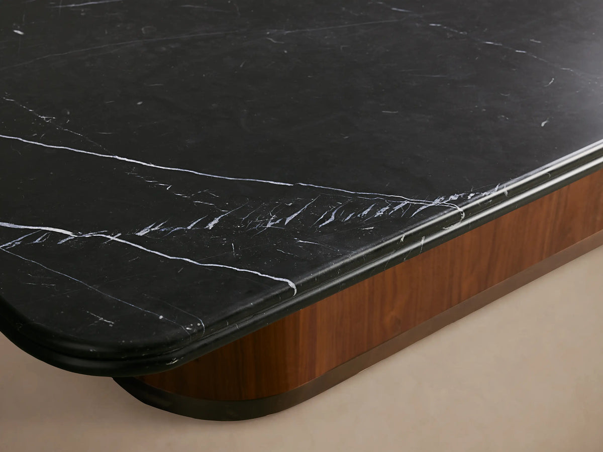 Caden Coffee Table: rectangular black stone top with rounded corners, walnut wood veneer base, antique bronze plinth on wood floor.