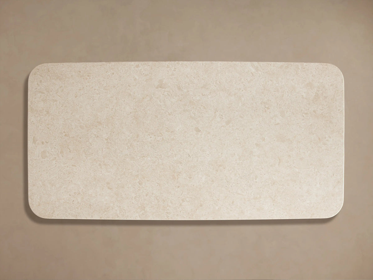 Close-up of Caden Coffee Table: textured cream stone top with rounded edge, resting on a dark walnut base.