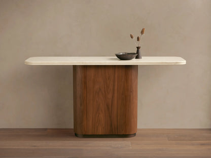 Caden Console Table with cream stone top and rounded walnut wood veneer base. A dark bowl and vase with dried plants sit on top.