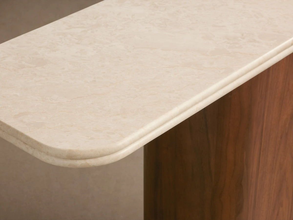 Caden Console Table with a cream stone top and a curved, dark walnut wood base featuring an antique bronze plinth.