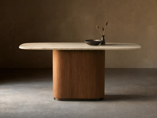 Caden Console Table with cream stone top and rounded walnut wood veneer base. A dark bowl and vase with dried plants sit on top.