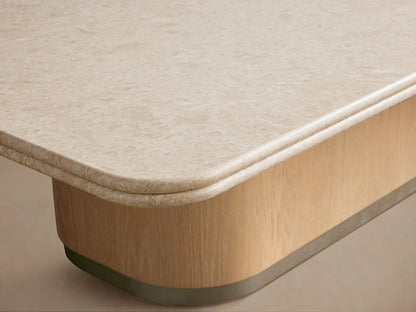 Caden Coffee Table. Cream stone top, rounded, over a light oak wood veneer base with brushed nickel plinth, on wood floor.