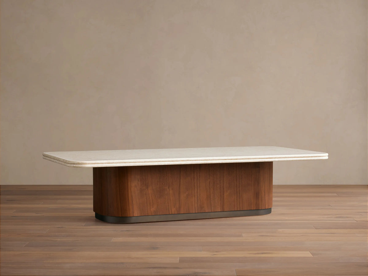 Caden Coffee Table: Rectangular cream stone top with rounded corners, walnut wood base, antique bronze plinth on wood floor.