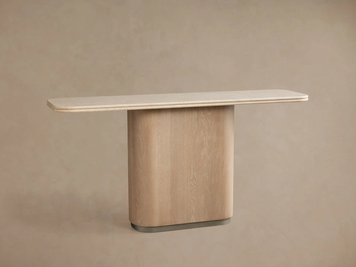 Caden Console Table with sand-finished oak base, brushed nickel plinth, and cream stone top, centered against a beige wall.