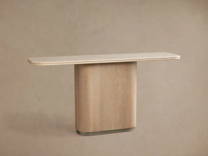 Caden Console Table with sand-finished oak base, brushed nickel plinth, and cream stone top, centered against a beige wall.