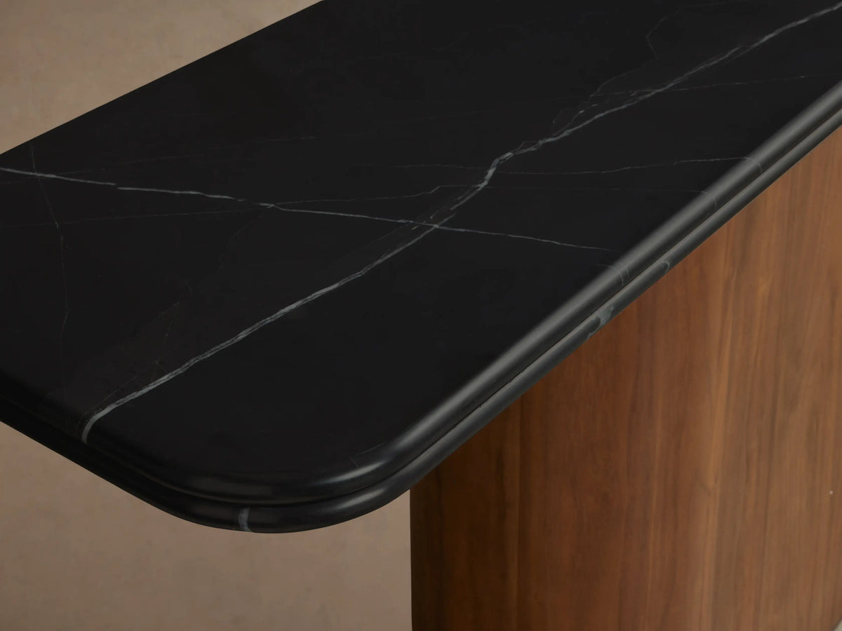 Caden Console Table, angled view. Features a black stone top with rounded edges on a vertical walnut wood base & dark plinth.