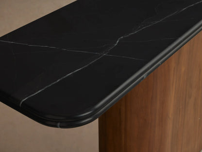 Caden Console Table, angled view. Features a black stone top with rounded edges on a vertical walnut wood base & dark plinth.