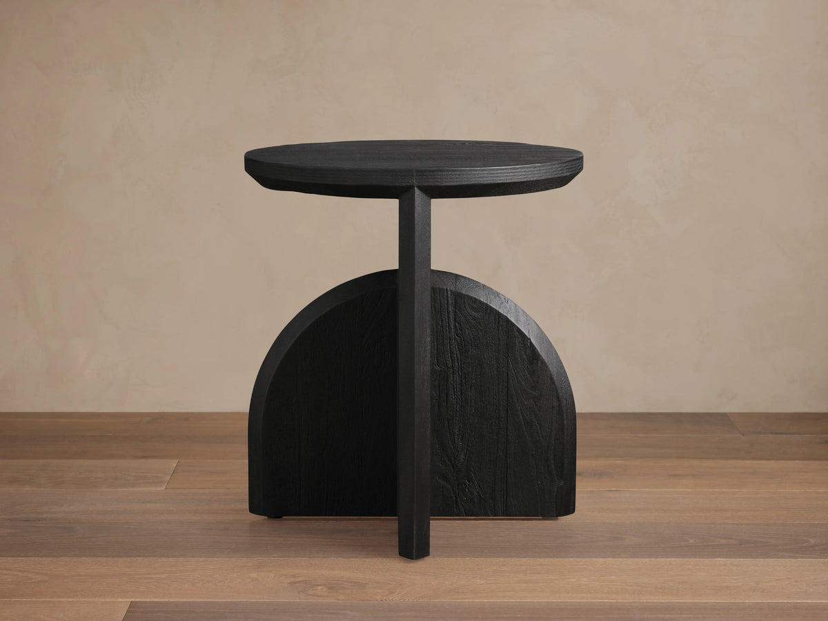 Calderone End Table in matte black finish, featuring a round top and semi-circular base on wooden floor.