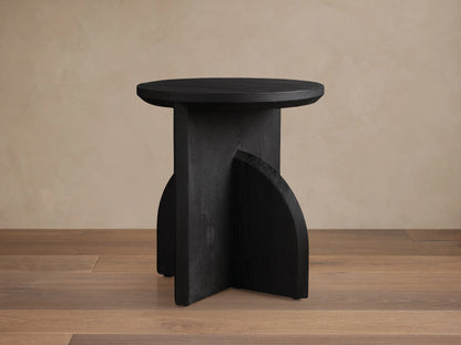 Calderone End Table with round tabletop, crafted from matte black mango wood, showcasing wood grain and geometric base design.