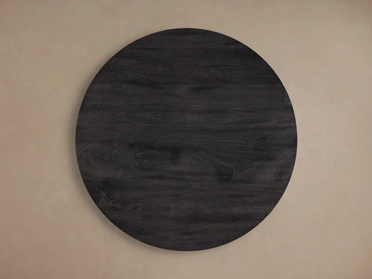 Calderone Coffee Table with round surface in matte black finish, highlighting grain patterns on solid mango wood, resting on sturdy legs.