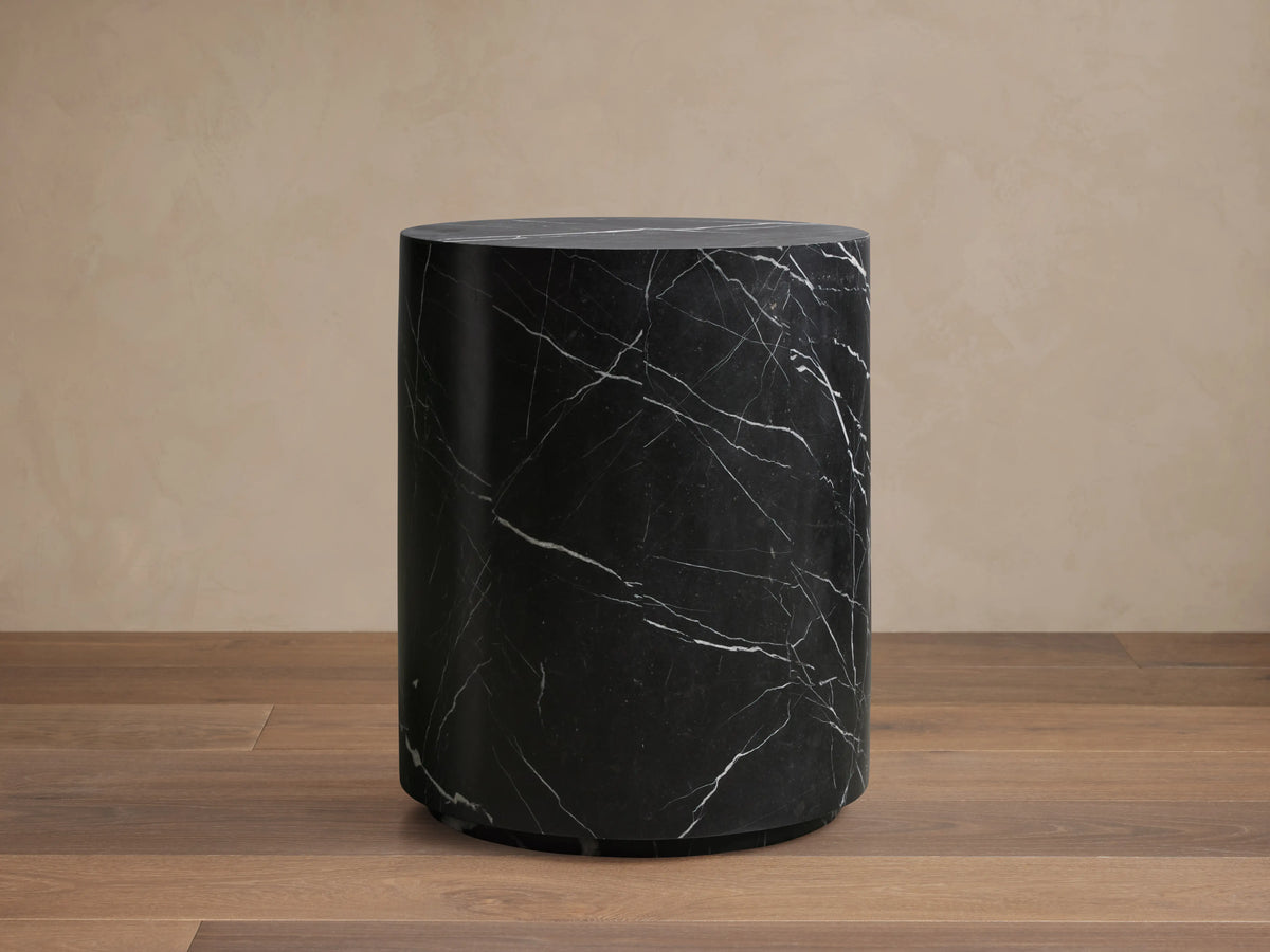 Cylindrical Cinzia Stone End Table made of black marble with white veining, featuring a smooth, polished surface on a wooden floor.