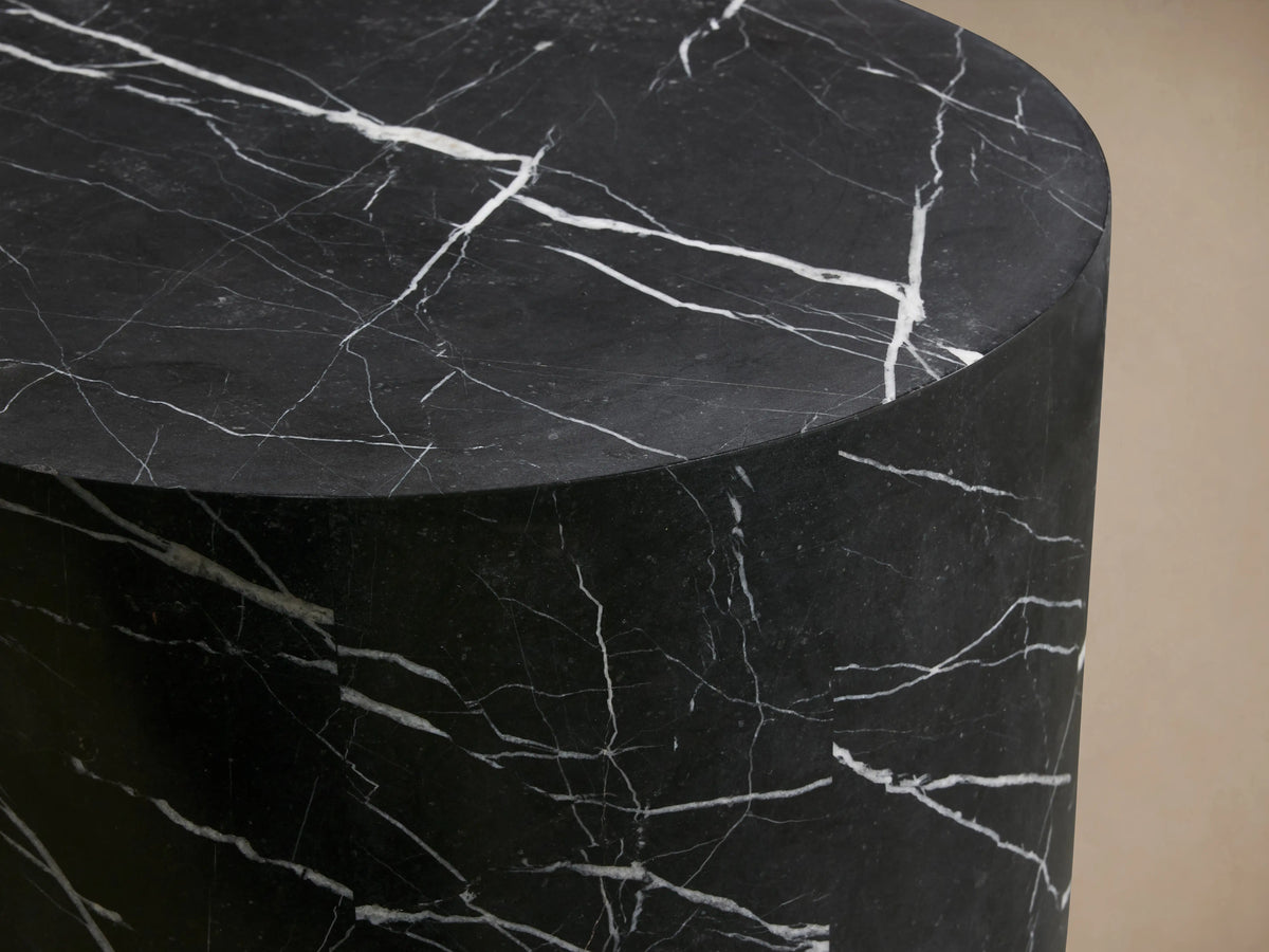 Cylindrical Cinzia Stone End Table made of black marble with white veining, featuring a smooth, polished surface on a wooden floor.