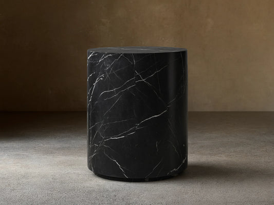 Cylindrical Cinzia Stone End Table made of black marble with white veining, featuring a smooth, polished surface on a wooden floor.