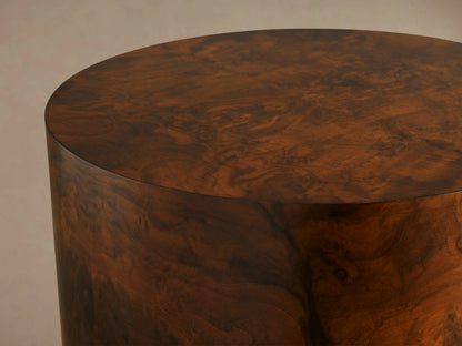 Cylindrical Cinzia Burl End Table in walnut burl wood with bookmatched pattern and plinth-style base on wood floor.
