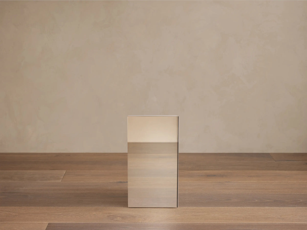 Chrome Cinzia Pedestal, a rectangular side table with a plinth base, next to a white furry chair.