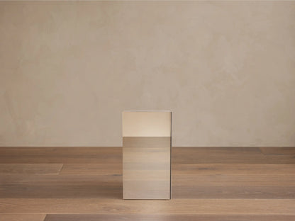 Chrome Cinzia Pedestal, a rectangular side table with a plinth base, next to a white furry chair.