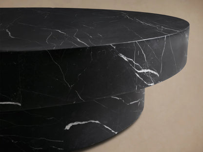 Cinzia Stone Round Coffee Table in black marble with white veining, featuring a low-profile, plinth-style base on a wood floor.