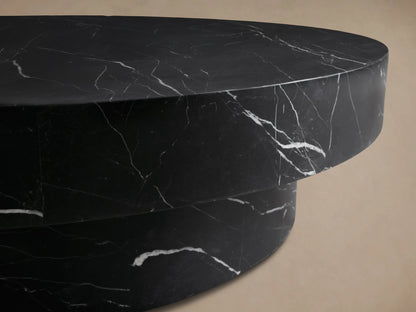 Cinzia Stone Round Coffee Table in black marble with white veining, featuring a low-profile, plinth-style base on a wooden floor.