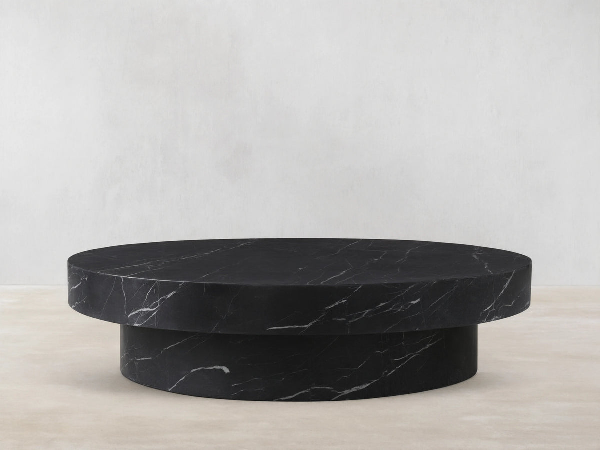 Cinzia Stone Round Coffee Table in black marble with white veining, featuring a low-profile, plinth-style base on a wood floor.