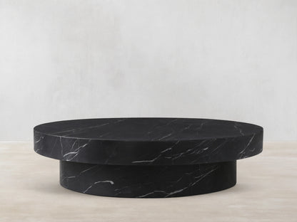 Cinzia Stone Round Coffee Table in black marble with white veining, featuring a low-profile, plinth-style base on a wood floor.