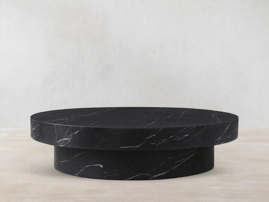 Cinzia Stone Round Coffee Table in black marble with white veining, featuring a low-profile, plinth-style base on a wood floor.