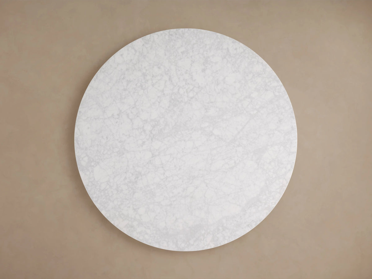 Cinzia Stone Round Coffee Table with a circular marble top and plinth-style base. Light gray tones, natural veining, on wooden floor.