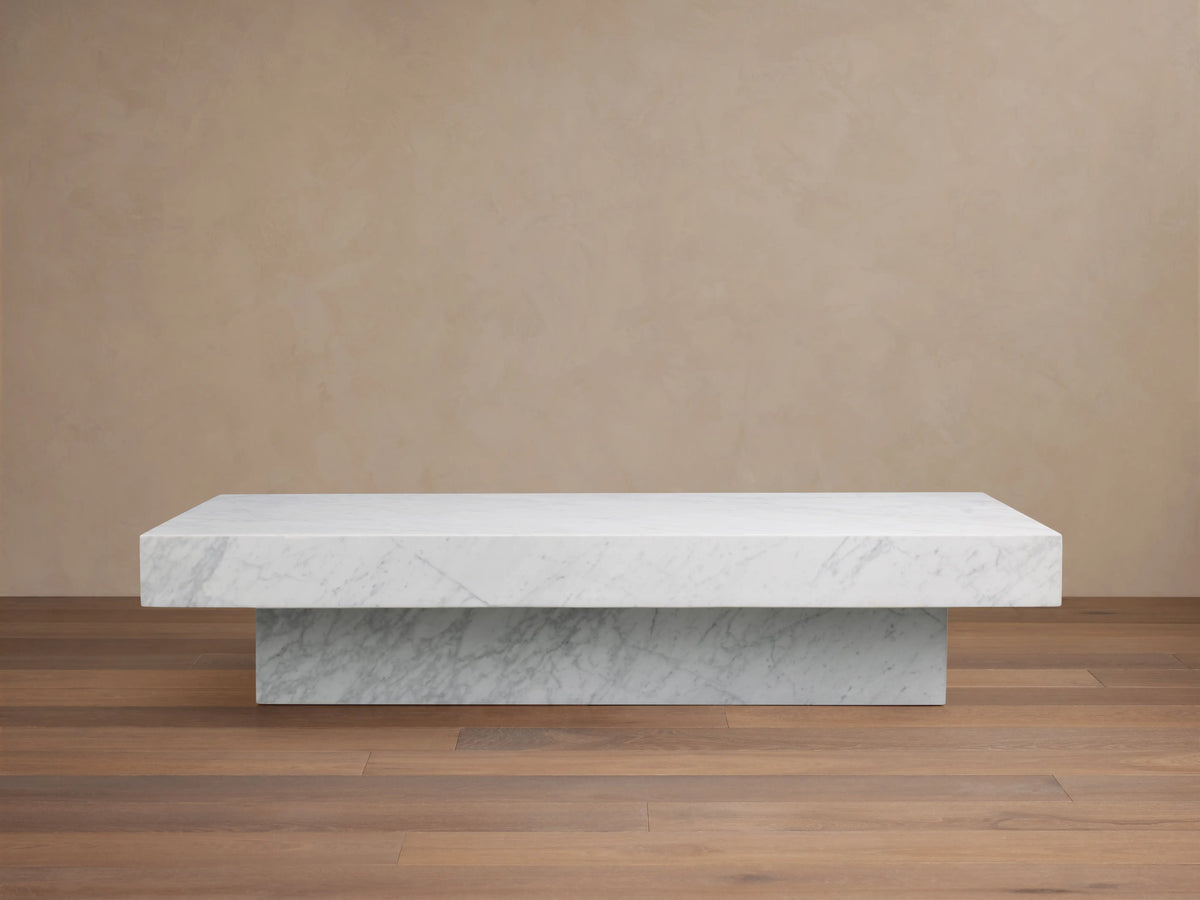 Cinzia Stone Coffee Table with a low-profile rectangular design, crafted from white marble, featuring subtle veining, on a wooden floor.